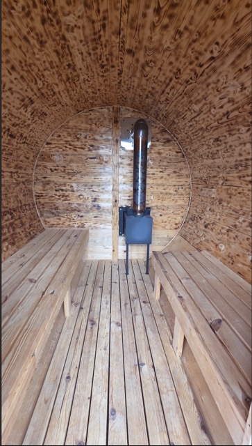 Interior of a Cedar Ridge barrel sauna with pine benches and a wood-burning stove