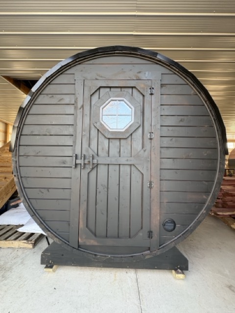 End face of a dark-stained Cedar Ridge barrel sauna with octagonal window door, inside a workshop