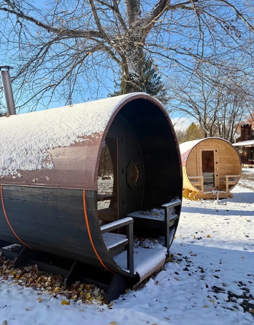 Two Cedar Ridge barrel saunas side by side in a snowy yard — dark-stained and natural pine
