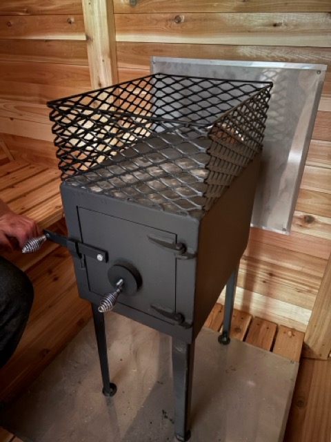 Wood-burning sauna stove with metal mesh stone basket inside a cedar-walled Cedar Ridge sauna