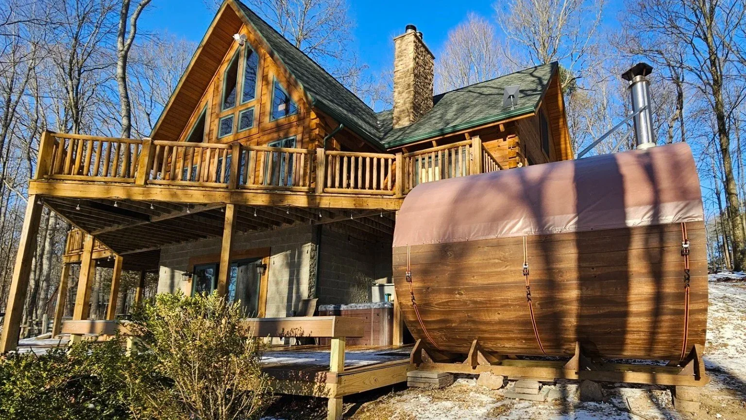 Cedar Ridge barrel sauna beside a log cabin in winter — ideal for vacation rental properties